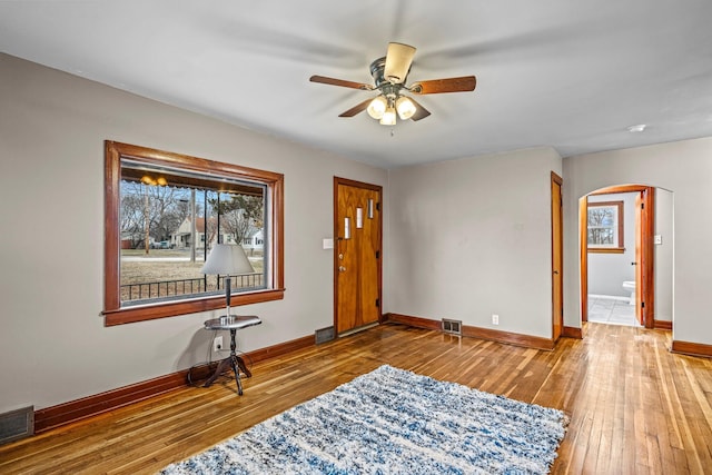 entrance foyer with arched walkways, visible vents, hardwood / wood-style floors, a ceiling fan, and baseboards