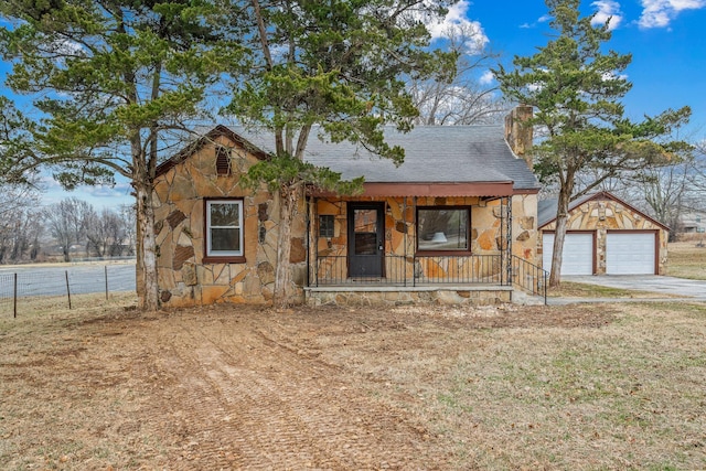 chalet / cabin featuring stone siding, a chimney, a detached garage, an outbuilding, and covered porch