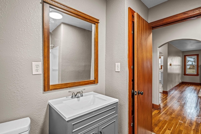 bathroom with baseboards, a textured wall, toilet, wood-type flooring, and vanity