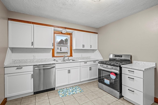 kitchen with tasteful backsplash, appliances with stainless steel finishes, light tile patterned flooring, white cabinetry, and a sink