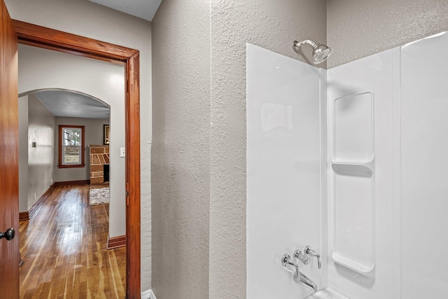 bathroom with baseboards, a shower, hardwood / wood-style floors, and a textured wall