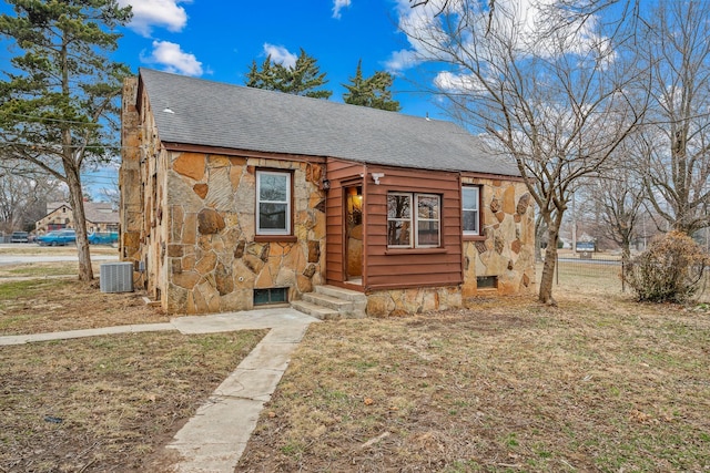 view of front of home with entry steps, central air condition unit, stone siding, roof with shingles, and a front yard