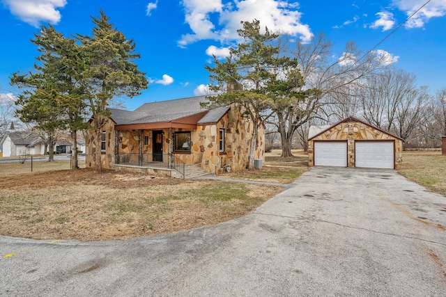 view of front of house featuring an outbuilding, a detached garage, a porch, a shingled roof, and stone siding