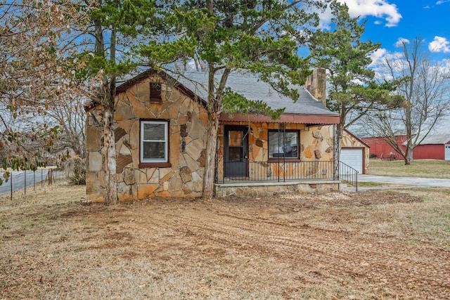 rustic home featuring a garage, driveway, stone siding, a chimney, and covered porch