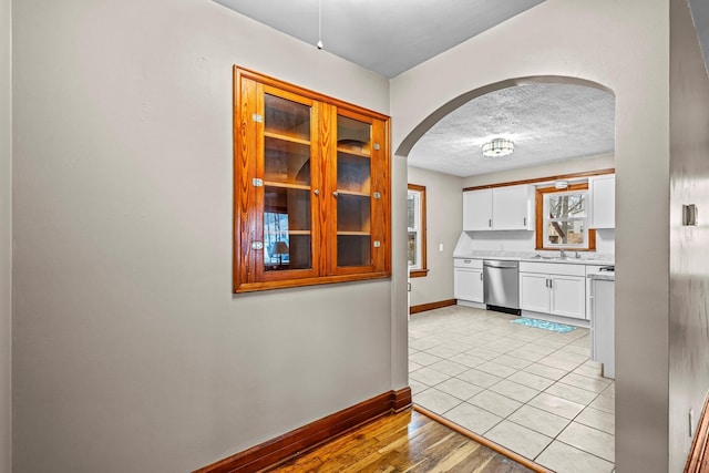 kitchen with a textured ceiling, arched walkways, white cabinets, light countertops, and dishwasher