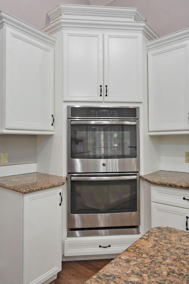 kitchen with stainless steel double oven, white cabinets, and dark stone countertops