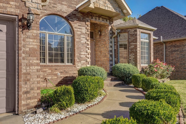 doorway to property featuring brick siding and roof with shingles