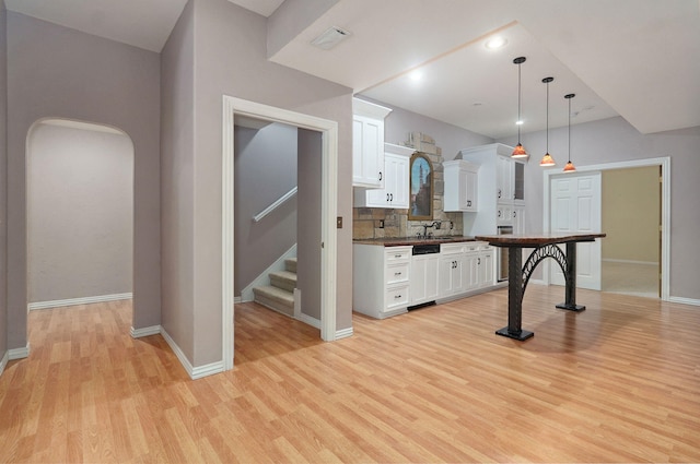 kitchen with hanging light fixtures, decorative backsplash, paneled dishwasher, white cabinets, and light wood-type flooring