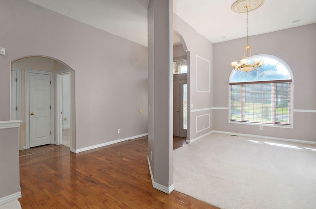 carpeted spare room featuring arched walkways, a chandelier, wood finished floors, and baseboards