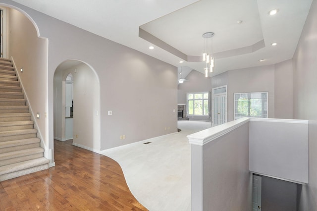 corridor with arched walkways, recessed lighting, a raised ceiling, wood finished floors, and baseboards