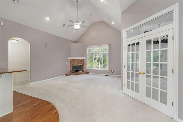 unfurnished living room featuring arched walkways, a glass covered fireplace, carpet flooring, french doors, and high vaulted ceiling