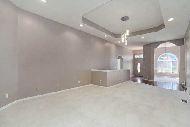 carpeted spare room with arched walkways, a chandelier, visible vents, baseboards, and a tray ceiling