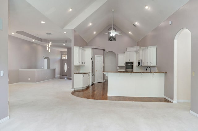 kitchen featuring arched walkways, high vaulted ceiling, stainless steel appliances, a peninsula, and white cabinetry