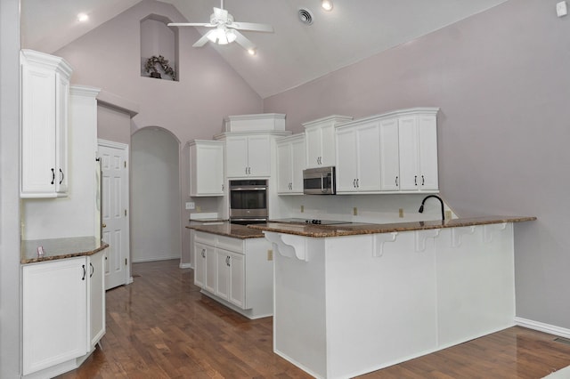 kitchen featuring arched walkways, visible vents, appliances with stainless steel finishes, white cabinetry, and dark stone counters