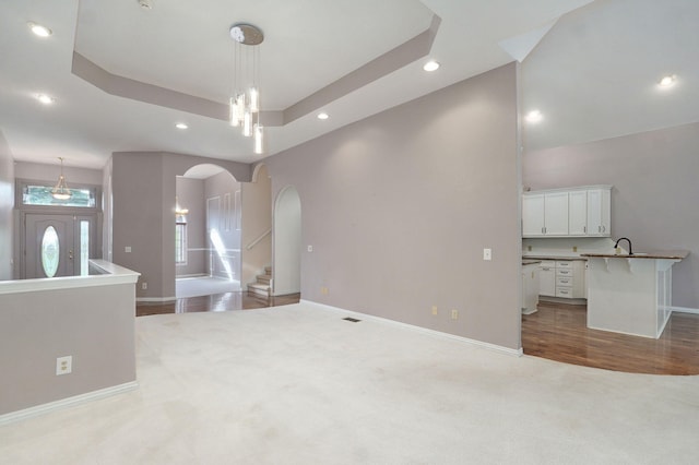 unfurnished living room featuring a tray ceiling, carpet flooring, arched walkways, and baseboards