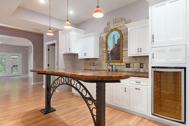 kitchen featuring wine cooler, arched walkways, white cabinets, and backsplash