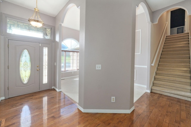 foyer entrance featuring arched walkways, hardwood / wood-style floors, stairway, and baseboards