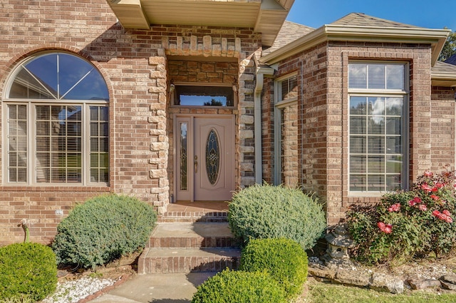 doorway to property featuring a shingled roof and brick siding