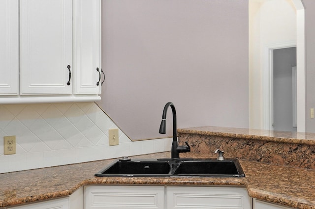 kitchen featuring tasteful backsplash, arched walkways, white cabinets, and a sink