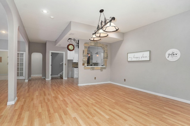 unfurnished living room featuring arched walkways, light wood-type flooring, stairs, and baseboards