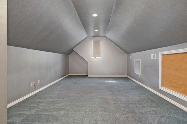 additional living space with lofted ceiling, a textured ceiling, carpet flooring, and visible vents