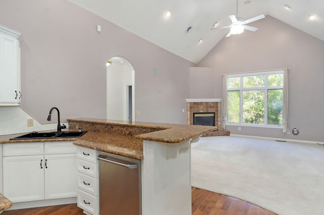 kitchen with a tile fireplace, a peninsula, a sink, open floor plan, and dark stone counters