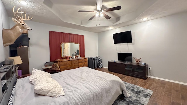 bedroom featuring baseboards, a tray ceiling, ceiling fan, and wood finished floors