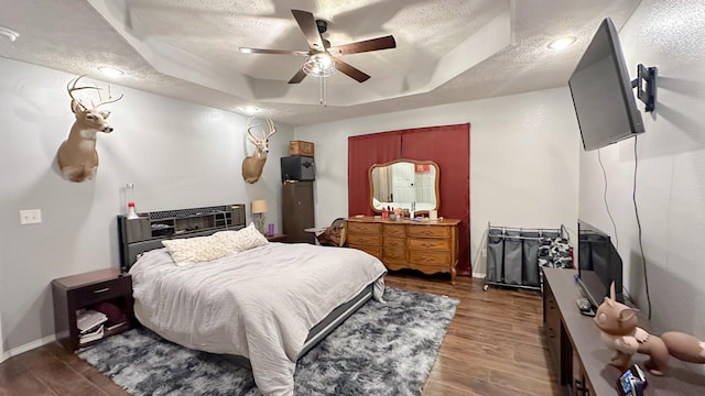 bedroom featuring a textured ceiling, wood finished floors, a raised ceiling, and baseboards