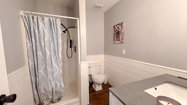 bathroom featuring toilet, visible vents, vanity, wainscoting, and a stall shower