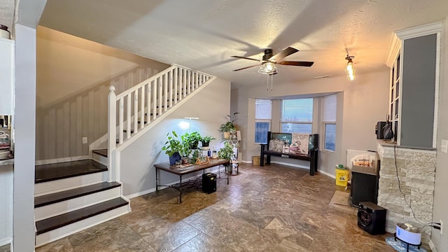 foyer with stairs, a textured ceiling, a ceiling fan, and baseboards