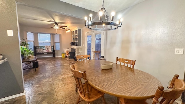 dining space featuring ceiling fan with notable chandelier, stone finish flooring, french doors, and baseboards