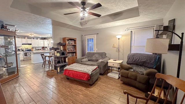 living area featuring light wood-style flooring, a raised ceiling, a textured ceiling, and a ceiling fan