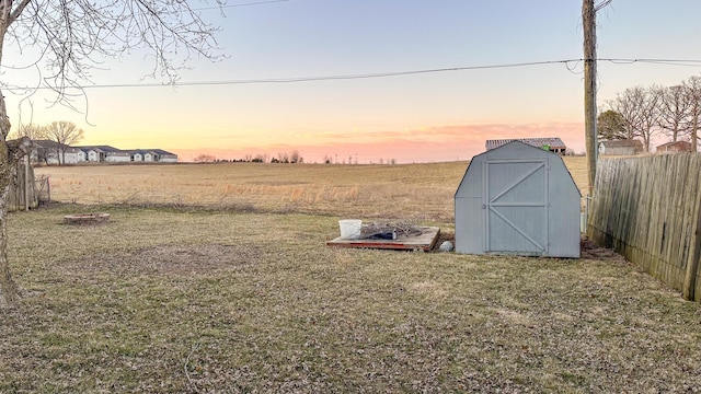 yard at dusk with fence, an outdoor structure, and a storage unit