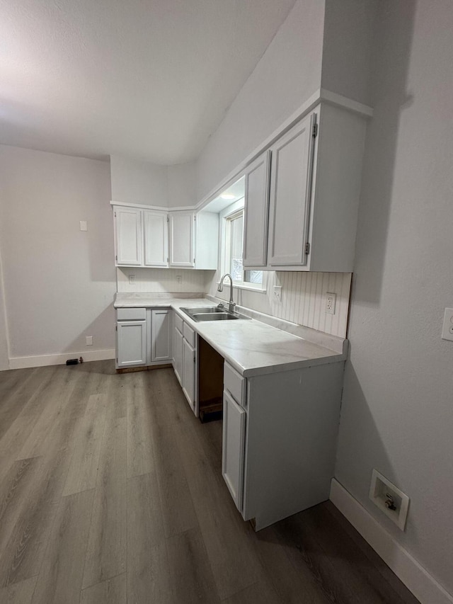 kitchen with dark wood finished floors, light countertops, white cabinetry, a sink, and baseboards