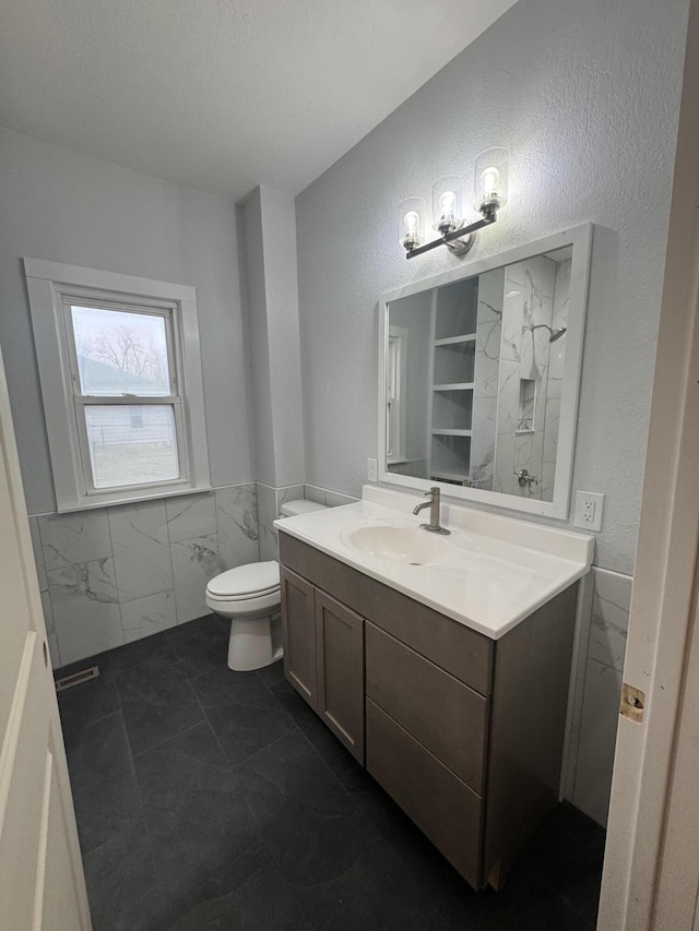 bathroom featuring toilet, wainscoting, tile walls, and vanity