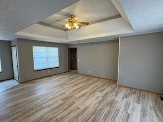 unfurnished room with a textured ceiling, a tray ceiling, wood finished floors, and a ceiling fan