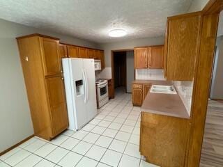 kitchen featuring light tile patterned floors, a textured ceiling, white appliances, light countertops, and brown cabinets