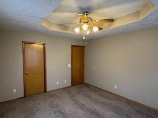 unfurnished bedroom featuring a textured ceiling, ceiling fan, a tray ceiling, and carpet flooring