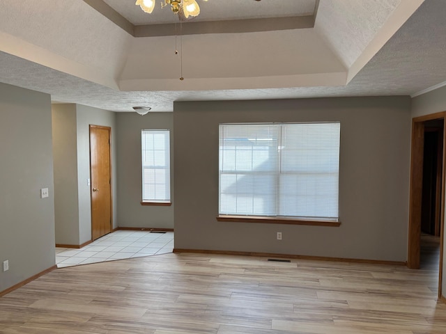 unfurnished room with a textured ceiling, light wood-type flooring, a raised ceiling, and visible vents