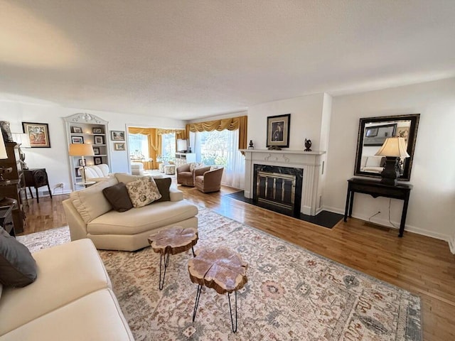 living area with a textured ceiling, baseboards, wood finished floors, and a high end fireplace