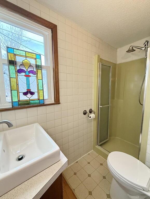 full bathroom with a shower stall, a textured ceiling, tile walls, and vanity