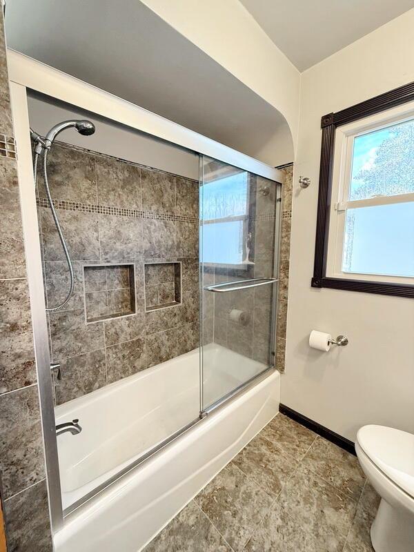 full bathroom with toilet, baseboards, and combined bath / shower with glass door