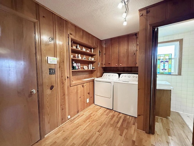 laundry area featuring washing machine and dryer, cabinet space, a textured ceiling, and light wood finished floors