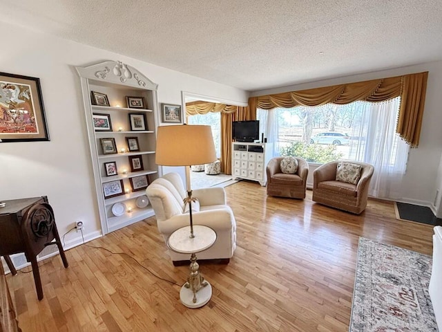 living area with light wood-type flooring, a textured ceiling, and baseboards