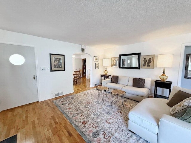 living room featuring arched walkways, visible vents, a textured ceiling, and wood finished floors