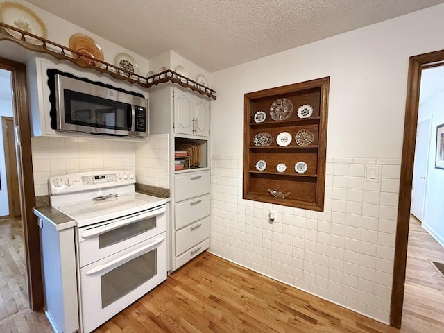 kitchen featuring tile walls, light wood finished floors, stainless steel microwave, a textured ceiling, and double oven range