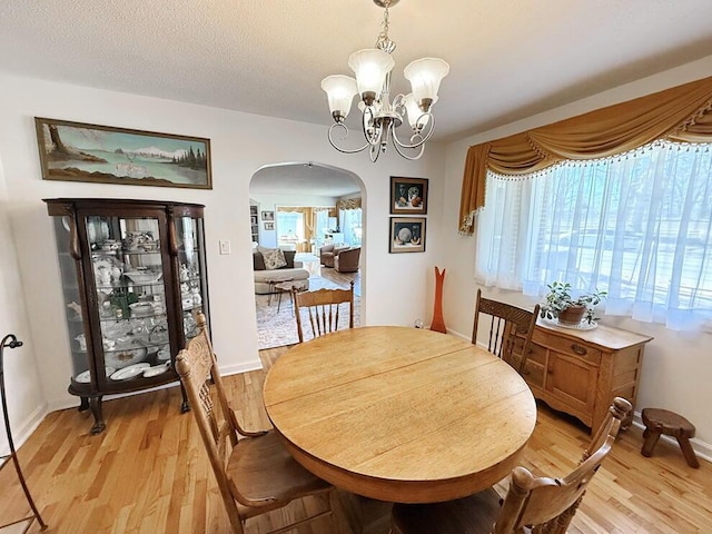 dining room featuring light wood-type flooring, an inviting chandelier, a healthy amount of sunlight, and arched walkways