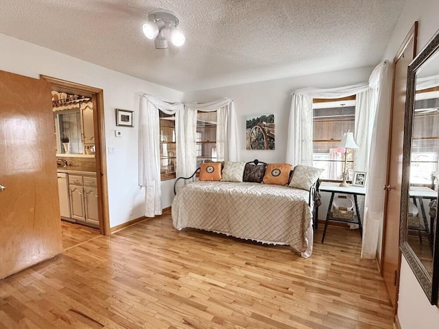 bedroom with light wood-style flooring, a textured ceiling, and ensuite bathroom