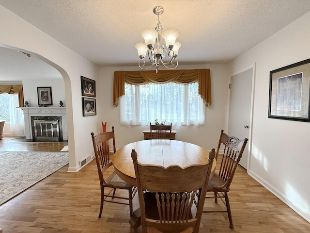 dining area featuring visible vents, a textured ceiling, light wood-type flooring, a chandelier, and a high end fireplace