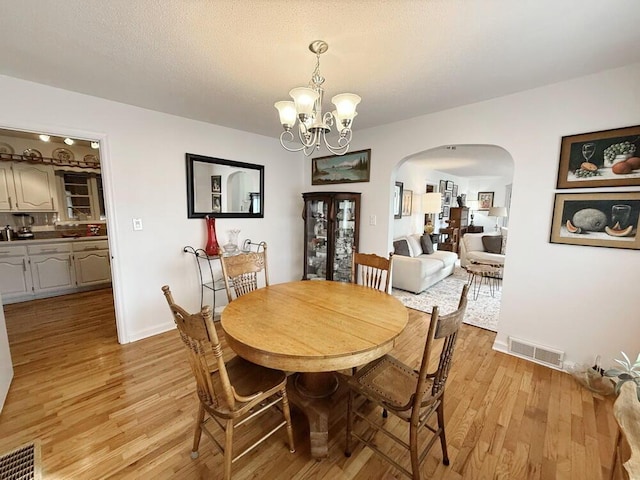 dining room featuring arched walkways, light wood-style flooring, visible vents, and a notable chandelier